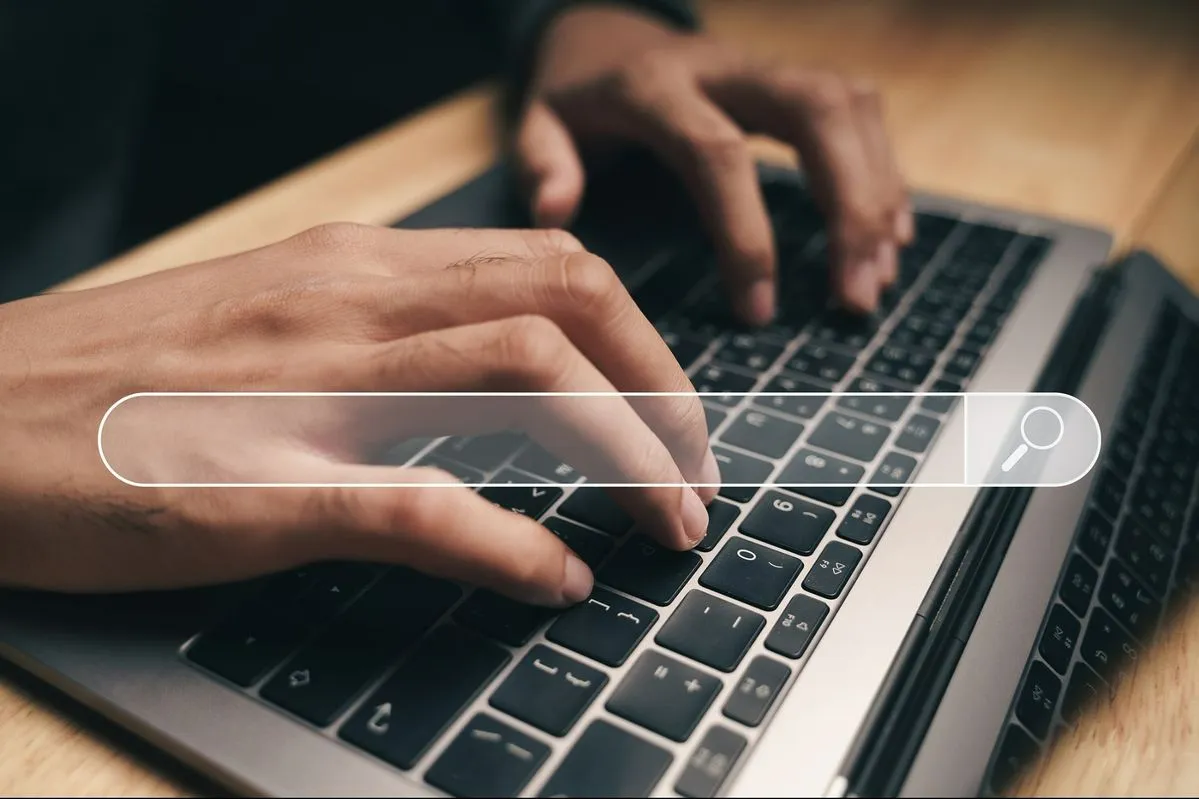 Handen die typen op een laptop met een zoekbalk-overlay